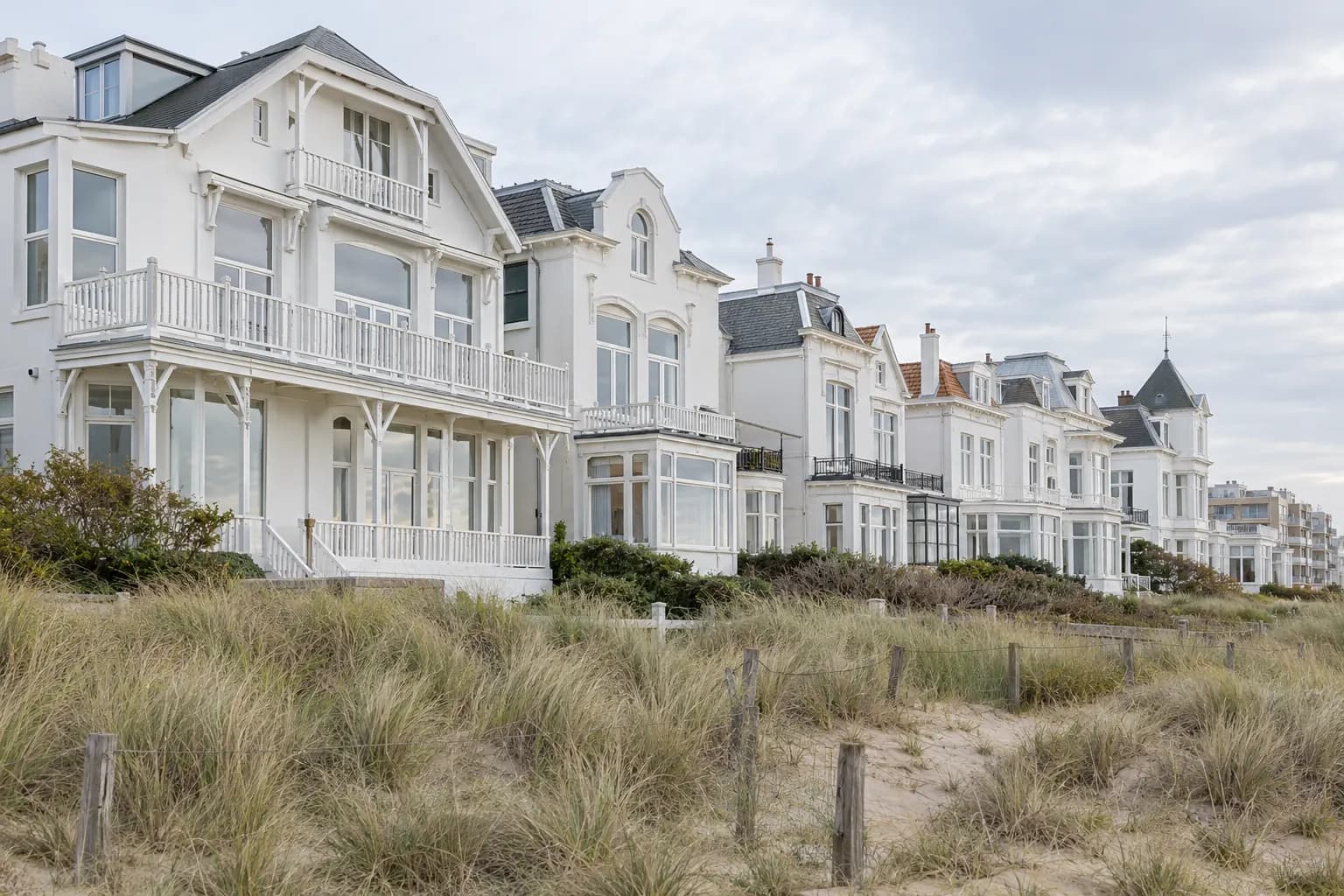 Appartementengebouwen en woonhuizen aan de kust bij Scheveningen met duingras op de voorgrond en een heldere zeelucht erboven